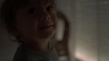 Cute little baby toddler opening automatic blinds in the morning, starting the day