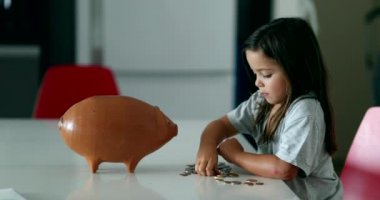 Little girl adding coins inside piggy bank. Child saving money concept