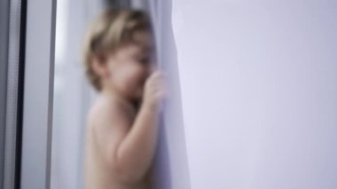 Blurred clip of toddler baby boy hiding behind curtain playing hide and seek