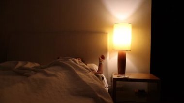 Woman getting out of bed in the middle of the night. Person turning bedside lamp on