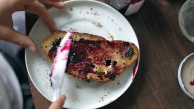 Hands putting jelly on toast, close-up person preparing breakfast bread