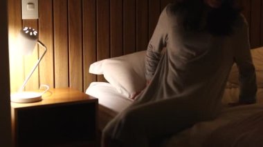 Woman lying in bed at night and turning bedside lamp off. Person going to sleep