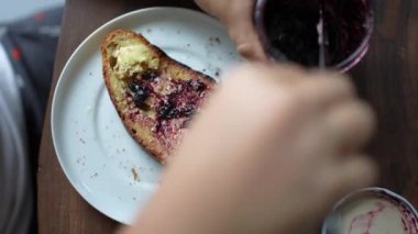 Hands putting jelly on toast, close-up person preparing breakfast bread