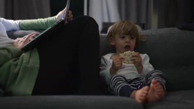 Mother in front of laptop at night sitting in sofa with infant