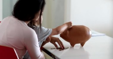 Mother and daughter financial savings adding coins inside piggy bank