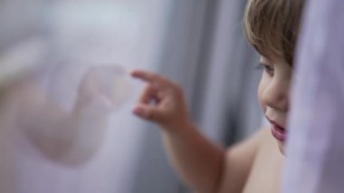 Toddler baby boy touching glass window with finger daydreaming
