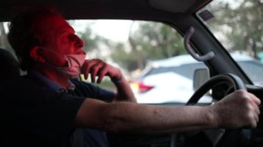 Older man stuck in red light removing covid-19 face mask while stopped in traffic