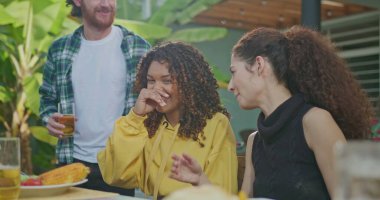 Bir grup arkadaş güneşli bir öğleden sonra barbeküde eğleniyorlar. Masada oturan herkes gülüyor ve mutlu..