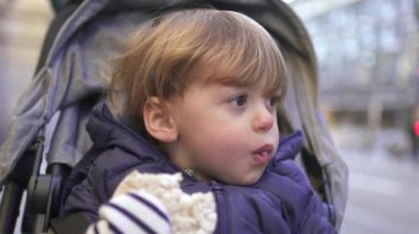 Baby toddler sitting inside stroller on city sidewalk