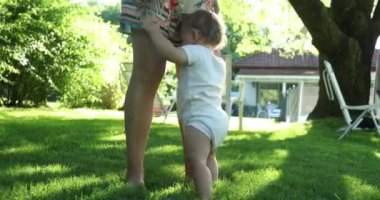 Adorable toddler baby infant holding on mother leg outside in backyard home