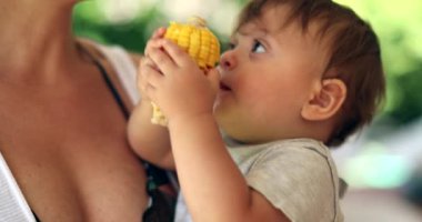 Adorable baby toddler holding corn cob offering to mother