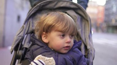 Baby toddler sitting inside stroller on city sidewalk