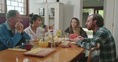 Aile kahvaltıda konuşuyor. Yetişkin kız ve erkek çocukları ile konuşan orta yaşlı evli bir çift. İnsanlar kahvelerini yudumluyor, sohbet ediyorlar.