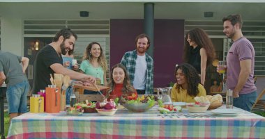 Bir grup mutlu insan evlerinin arka bahçesindeki barbeküde oturuyor. Arkadaşların ailesi öğle yemeği için toplandı.