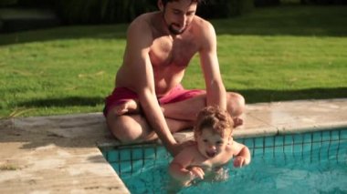 Anne ve babası bir yaşında bir erkek çocuğu yüzme havuzunda tutuyor.