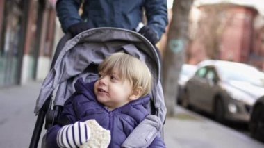Baby toddler sitting inside stroller on city sidewalk