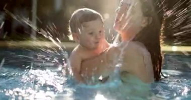 Mother caring and holding baby child at the pool. Infant toddler splashing water everywhere