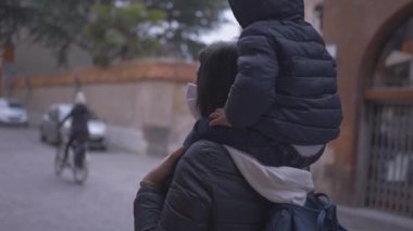 Mother walking outside with toddler in back wearing covid face mask