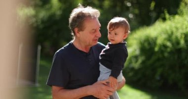 Grand-father holding one year old baby infant toddler in arms outdoors
