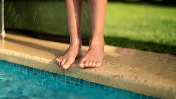 若い男の子の足はプールサイドの端に立っている 子供がプールの水に飛び込む — ストック動画