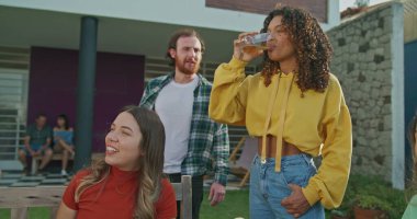 Bir grup arkadaş arka bahçede öğle yemeği yiyor. Çeşitli insanlar bahçe partisinde sohbet ediyorlar.