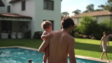 Parent holding baby infant in swimming pool outdoor home garden setting