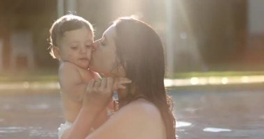 Mother caring for baby at the swimming pool kissing on the cheek, mom kisses toddler