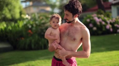 Young father holding baby son in swimming pool environment outdoors
