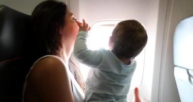 Baby reaching out to plane window. Mother traveling with infant son child
