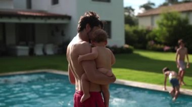 Father holding baby infant in home backyard swimming pool. Dad kissing toddler forehead