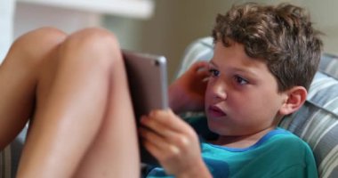 Çocuk kanepede tablet kullanıyor. İnternette oynayan ve internette gezinen samimi genç çocuk