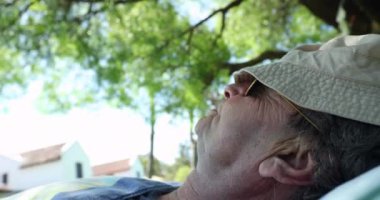 Relaxed older man asleep under a tree, senior man with face covered with hat