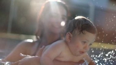 Baby toddler at the swimming pool water with mom. Mother holding teaching infant son to swim