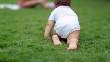 Dışarıda çimlerin üzerinde emekleyen şirin bir bebek. Sevimli çocuk ailesiyle birlikte dışarıda sürünüyor.