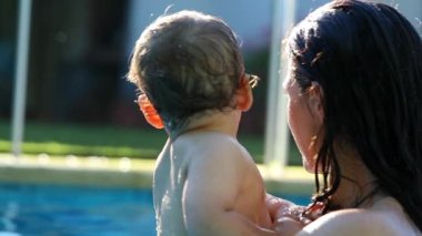 Candid real life mother holding baby infant toddler during summer day at the swimming pool water