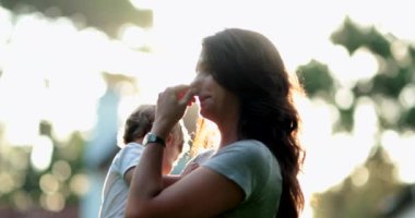 Samimi bir anne bebeğini tutarken yüzünü tırmalıyor, anne çocuğu öpüyor.