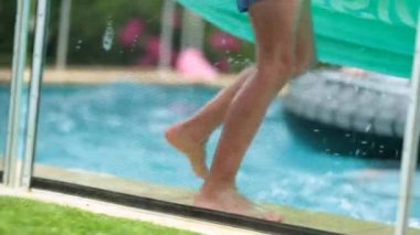 Havuzun kenarında yürüyen çocuk bacakları şişme yatak tutuyor.