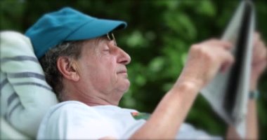 Older man reading newspaper outdoors. Senior person relaxing outside in nature