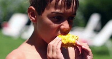 Dışarıda güneş ışığında mısır yiyen çocuk.