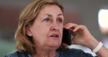 Candid senior lady speaking on phone at home