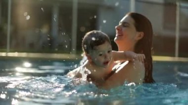 Mother holding happy baby infant son splashing water in slow-motion during summer day