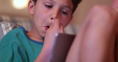 Geceleri tablet kullanırken yüzünü kaşıyan bir çocuk.