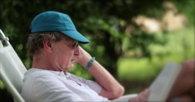 Candid senior man reading book story outdoors