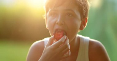 Küçük çocuk dışarıda sağlıklı meyve yiyerek altın saat içinde, kameraya gülümseyen çocuk portresi