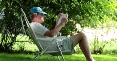 Senior man reading book outdoors, casual and candid older retired man holding book
