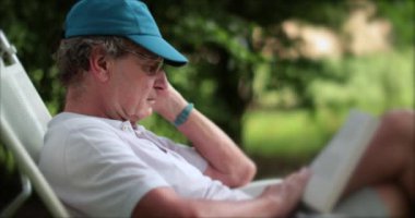 Dışarıda kitap okuyan yaşlı bir adam, 70 'li yaşlarda emekliliğin tadını çıkaran biri. 