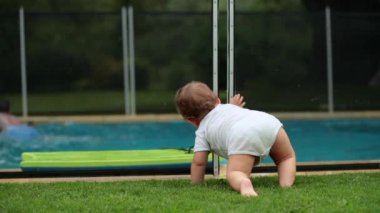 Havuz kenarındaki çitlerin yanında duran bebek. Havuzda oynayan çocuklar, çocuk gözlemleyen çocuklar.