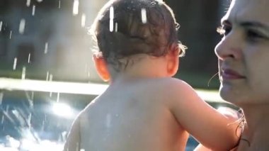 Mother and child baby together at the swimming pool during summer day in slow-motion dreamlike