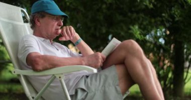 Senior man leaning outside reading book casually