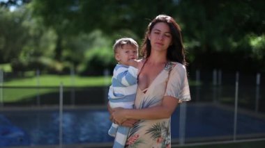 Mother in her 30s holding infant baby son outdoors in home backyard